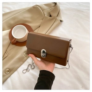 Detail of caramel crossbody box bag featuring silver twist lock and sleek metal chain strap