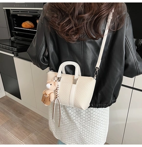 Detail of a beige small tote bag with crossbody strap and a cute plush bear pendant