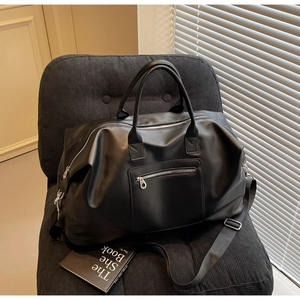 Détail du sac de voyage noir en texture cuir posé sur une chaise en velours