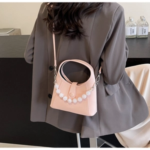 Detail of pink PU leather bucket bag with pearl strap worn by model in grey blazer