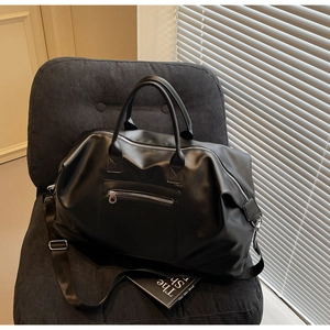 Détail du sac de voyage en cuir PU noir avec fermetures argentées sur un fauteuil chic
