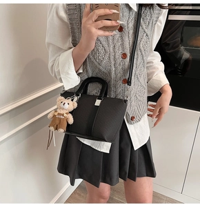 Close-up of black textured bucket bag with woven patterns and a cute bear charm