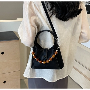 Detail of black leather bucket bag with decorative amber bead chain and metallic accents