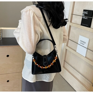 Detail of black leather bucket bag featuring amber beaded chain and adjustable shoulder strap
