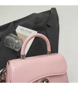 Dettaglio della borsa in pelle rosa lucida con chiusura a scatto e manico tondo