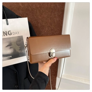 Detail of a brown leather box bag featuring a silver rotary lock and chain strap