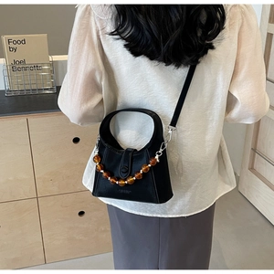 Detail of black leather crossbody bag featuring amber beaded handle and matte finish