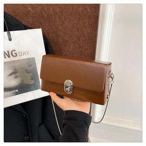 Close-up of a brown leather box bag with a silver cylinder lock and chain strap