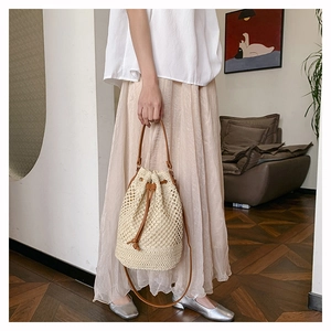 Detail of hand-woven straw bucket bag featuring brown leather drawstring and mesh texture