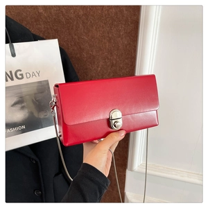 Detail of red minimalist box bag with silver twist lock and chain strap on a chic coat