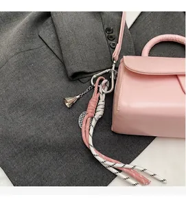 Dettaglio di una borsa rosa con ciondolo in corda intrecciata su una giacca grigio scuro