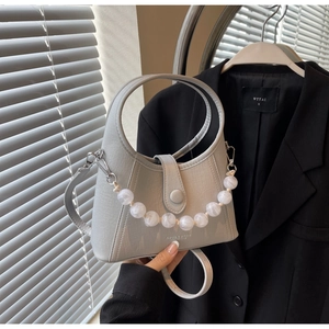 Detail of light gray beaded bucket bag with marble charms against a business suit