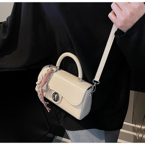 Detail van een crèmewitte crossbodytas met zijden sjaalbedeltje en metalen draaisluiting