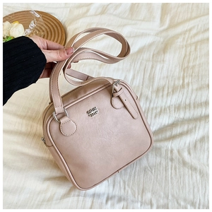 Close-up of a nude square underarm bag with metal logo and dual strap detail
