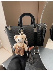 Black woven bucket bag with smooth leather handles and a cute plush bear charm