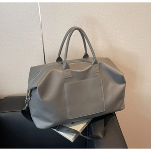 Détail du sac de voyage en cuir mat gris avec poignées posé sur un canapé en cuir