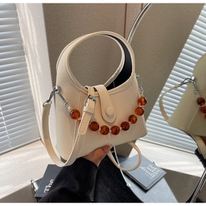 Detail of beaded handle on cream white PU leather bucket bag with mirror reflection