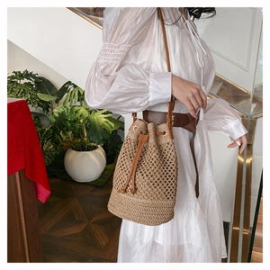 Detailed view of woven straw bucket bag with brown leather drawstring and shoulder strap