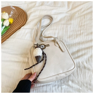 Detail shot of a cream white square shoulder bag with cute plush ice cream keychain charm