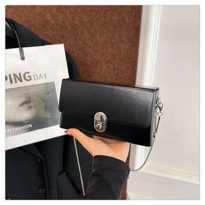 Detail of minimalist black box bag featuring silver oval metal lock and thin chain strap