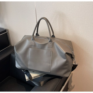 Gros plan d'un grand sac de voyage gris en cuir mat posé sur un canapé noir