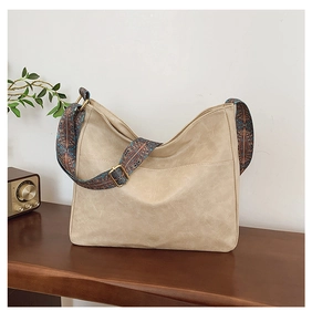 Close-up of beige tote bag with a wide ethnic pattern strap on a wooden table