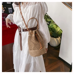Detail of woven straw bucket bag showing leather drawstring closure and round handle grip
