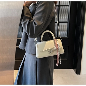 Detail van een witte rechthoekige crossbodytas met zilveren draaislot en geweven hanger