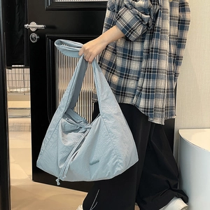 Detail of light blue nylon tote bag showing slouchy drawstring texture on model
