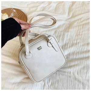 Detail of off-white leather square bag with silver metal logo and dual handles