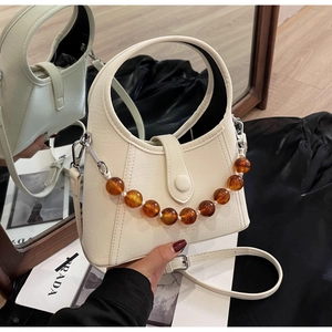Detail of cream white beaded bucket bag with amber chain and sleek integrated handle