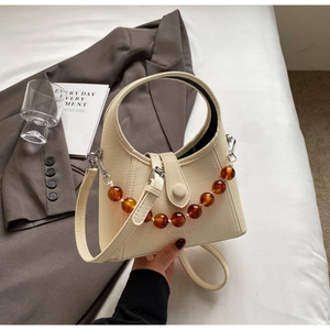 Detail of a beige trapezoid handbag with amber beaded chain and top handle grip