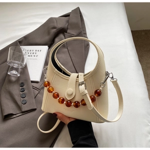 Detail of cream bucket bag with amber acrylic bead chain and wide arched handle