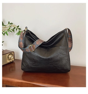 Detail of black faux leather hobo bag with vintage texture and wide patterned strap