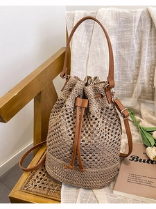 Woven straw bucket bag with brown leather trim and drawstring on a vintage chair