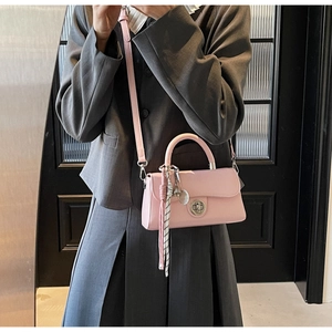 Detail van roze lederen crossbodytas met zilveren draaisluiting en bellenhanger accessoire