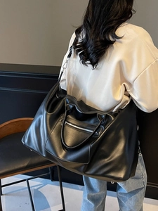 Grand sac de voyage en cuir noir porté à l'épaule dans un cadre d'intérieur minimaliste moderne