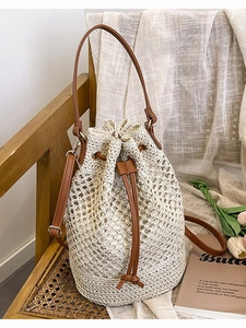 Woven straw bucket bag with brown leather drawstring and dual straps on a wooden chair