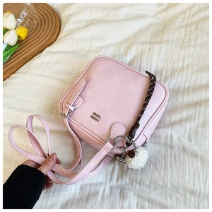 Detail of pink square shoulder bag with MOE HIQ logo and decorative pom-pom charm