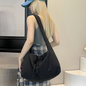 Detailed side view of a large black nylon crossbody bag with drawstring on a female model