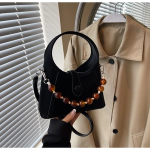 Close-up of black bucket bag with round handle and amber beaded decorative chain