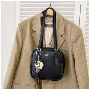 Close-up of black leather rectangular shoulder bag with silver lettering and plush charm