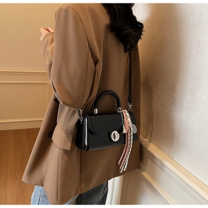 Detail van zwarte laklederen crossbodytas met zilveren sluiting en geweven hanger