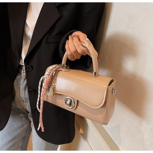 Detail van beige kunstlederen handtas met zilveren draaisluiting en geweven kwastje hanger