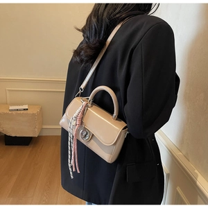 Detail van abrikooskleurige crossbodytas met zilveren draaisluiting en kwastje