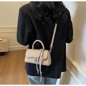 Detail van beige crossbodytas met zilveren draaisluiting en kleurrijke touwhanger