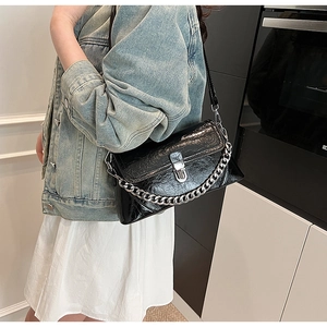 Close-up of black glossy faux leather bag featuring a silver chain and metal twist lock
