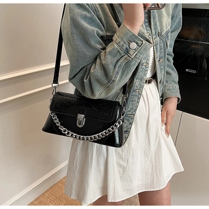 Detail of black faux leather crossbody bag with crocodile texture and silver chain