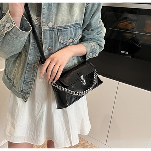 Detail view of black textured oil wax leather crossbody bag with chunky silver chain and lock