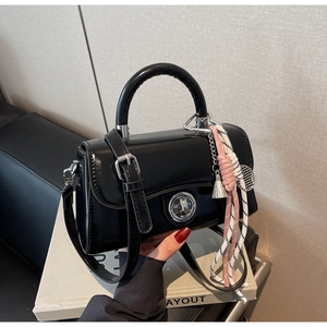 Detail van zwarte glanzende crossbodytas met zilveren draaisluiting en gevlochten hanger
